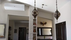 Uma sala de jantar com mesa de mármore, luminárias decorativas penduradas, lareira com um espelho ornamental acima e uma porta à direita.