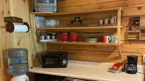 Cocina compacta con paredes de madera, un refrigerador pequeño, un microondas, dispensador de agua y cafetera.