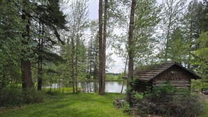 Una cabaña rústica junto a un lago, rodeada de árboles altos.