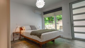 A modern bedroom with a large bed, a chair, and a view of a garden through a sliding glass door. - Modern 3 bedroom, 3 en suites, dog friendly loft in McKinley (Kelowna)