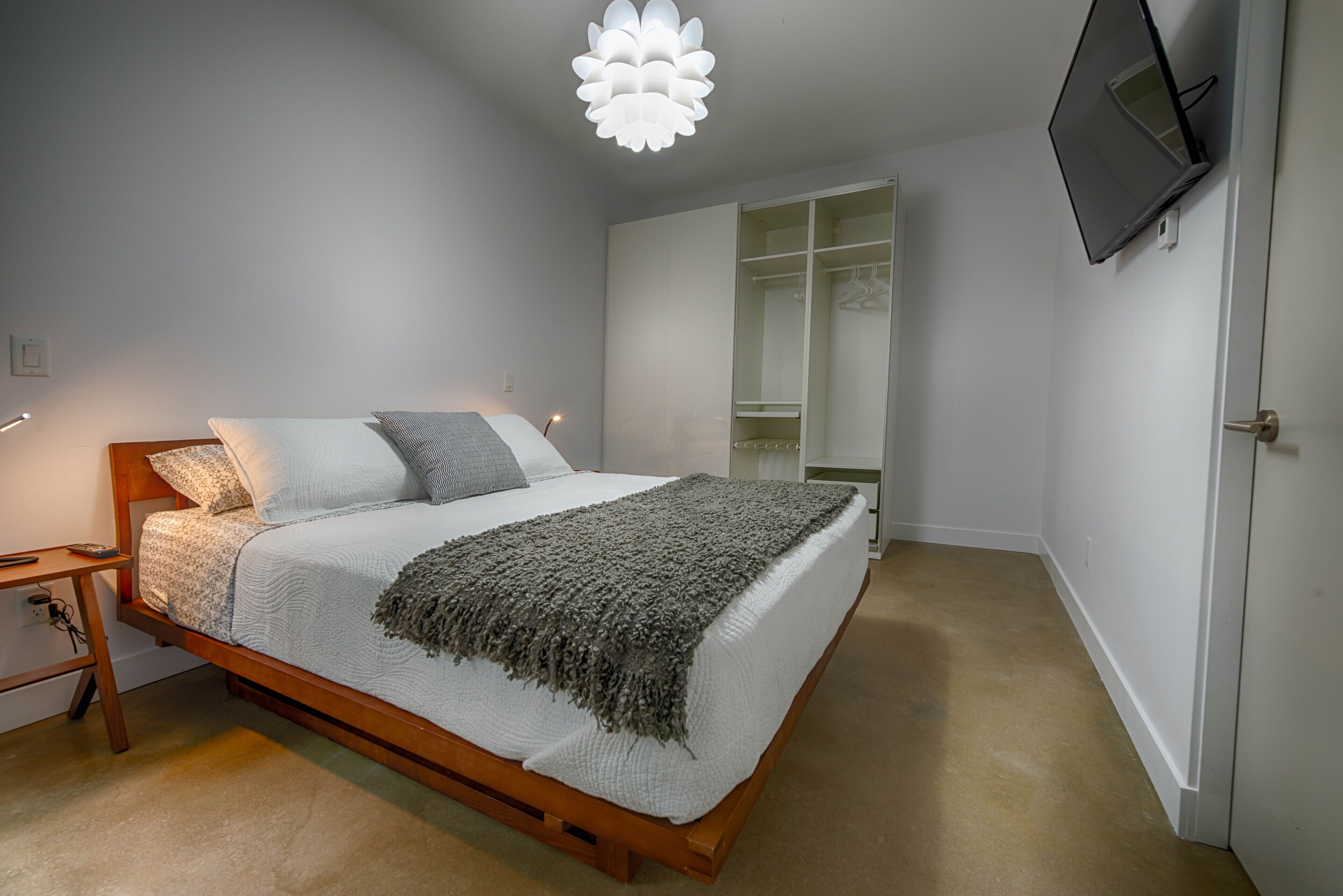 A bedroom with a wooden bed, a bedside table, a nightstand, a wardrobe, and a TV mounted on the wall.
