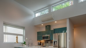 A modern kitchen with a central island, bar stools, a refrigerator, and a microwave. - Modern 3 bedroom, 3 en suites, dog friendly loft in McKinley (Kelowna)