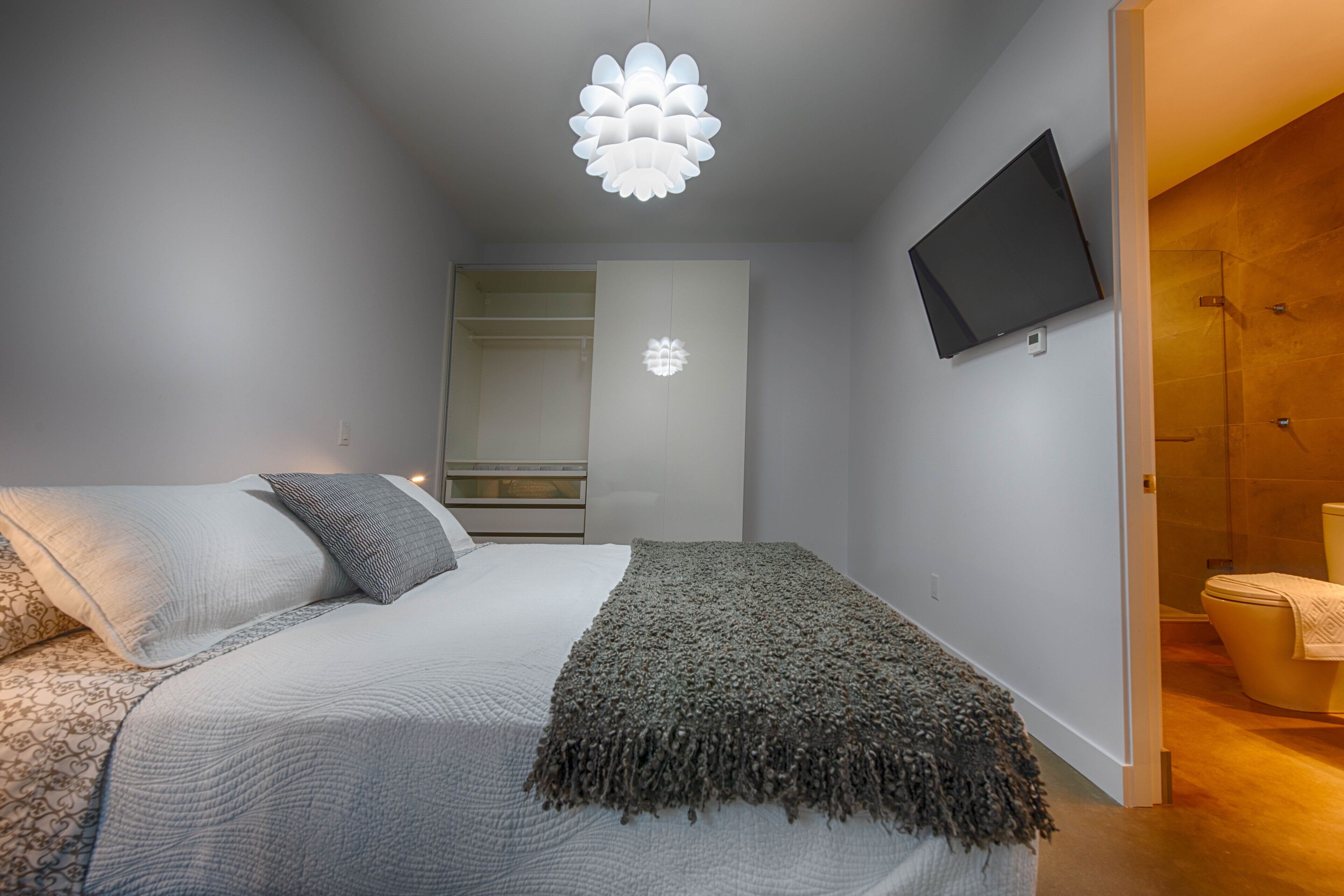 A modern bedroom with a bed, a TV mounted on the wall, and a closet.