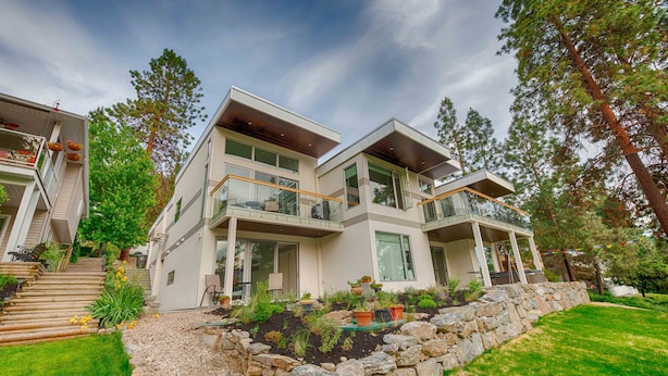 A modern two-story house with a stone retaining wall, a balcony, and a well-maintained garden. - Modern 3 bedroom, 3 en suites, dog friendly loft in McKinley (Kelowna)
