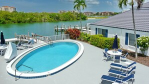 A swimming pool with lounge chairs and umbrellas, surrounded by greenery and a body of water. - Incredible Waterfront View, Pool, Dolphins, Fishing, Docks, Snook Inn 1 block up (Marco Island)