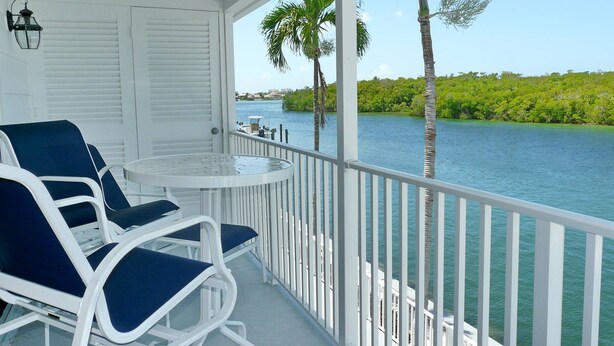 A balcony with white railings, two blue cushioned chairs, and a small round table. - Incredible Waterfront View, Pool, Dolphins, Fishing, Docks, Snook Inn 1 block up (Marco Island)