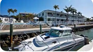 A marina with a boat docked near a building with a pool and palm trees. - Incredible Waterfront View, Pool, Dolphins, Fishing, Docks, Snook Inn 1 block up (Marco Island)
