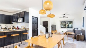 A modern kitchen with dark cabinets, a wooden dining table, and a large window overlooking a garden. - Casa Rosas - Private pool (Cabo San Lucas)