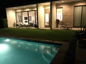 Ein modernes Haus mit Swimmingpool, Sitzgelegenheiten im Freien und einer Fassade aus Naturstein.