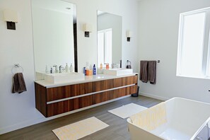 Ein modernes Badezimmer mit einem großen Spiegel, zwei Waschbecken, einer Holzausstattung und einer Badewanne.