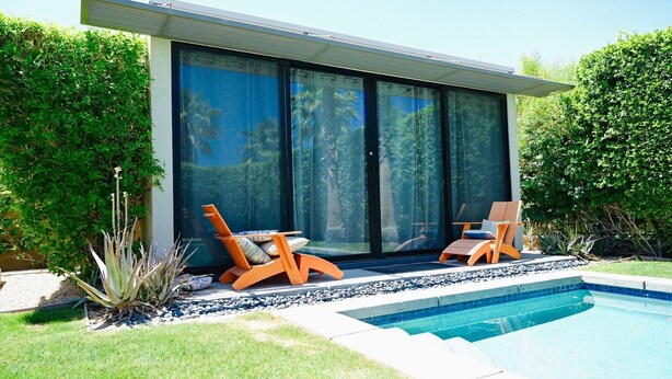 A modern house with a swimming pool, two orange lounge chairs, and a large sliding glass door. - Quiet and peaceful retreat (La Quinta)