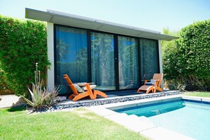 A modern house with a swimming pool, two orange lounge chairs, and a large sliding glass door.