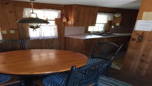 A wooden dining table with chairs, a chandelier, and a kitchen area with a sink and cabinets. - Old Cape Cod Charm in Chatham MA, 1/4 mile Walking Distance to Hardings Beach (Chatham)