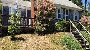 A two-story house with a front porch, a small garden with pink flowers, and a wooden staircase leading to the front door. - Old Cape Cod Charm in Chatham MA, 1/4 mile Walking Distance to Hardings Beach (Chatham)