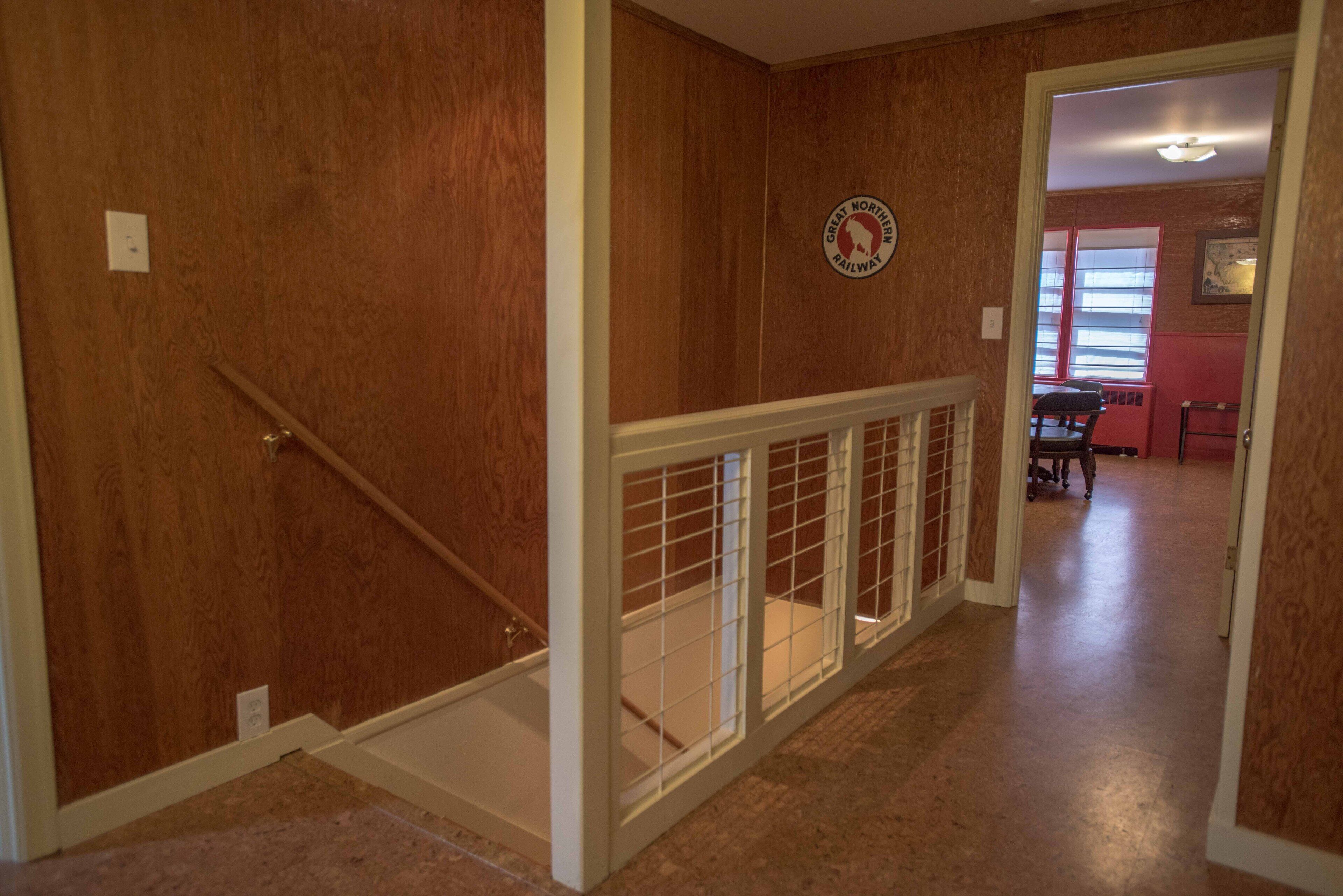 A wooden hallway with a white railing, a Great Northern Railway sign, and a glimpse of a dining area in the background.