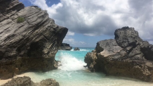 Una playa rocosa con agua turquesa cristalina y un cielo nublado.