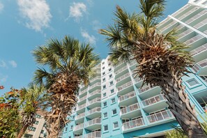 Un hôtel à plusieurs étages, doté de balcons et bordé de palmiers.