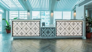 Un espace d’accueil au design moderne, avec un parquet en bois disposé en chevrons, un séparateur aux motifs géométriques et une vue sur le paysage urbain grâce à de grandes fenêtres.