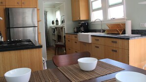 A compact kitchen with wooden cabinets, a stainless steel refrigerator, and a dining area with a table and chairs. - Charming North Park house, with parking and new central Air.  (San Diego)