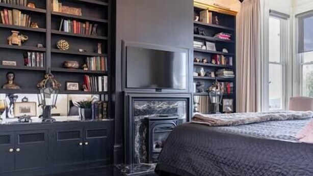 A bedroom with a fireplace, a large bookshelf, and a bed with a quilt.