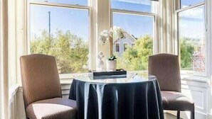 A room with two chairs and a table, large windows, and a view of greenery and a house.