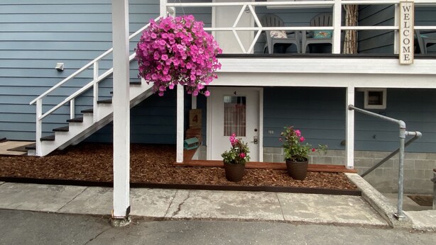 A two-story building with a welcoming sign, a staircase, and potted plants.
