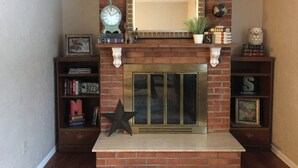 A brick fireplace with a large mirror above it, flanked by shelves with books and decorative items.