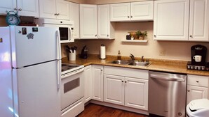 A modern kitchen with white cabinets, a stainless steel sink, a dishwasher, and a coffee maker.