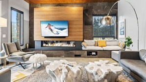 Ein modernes Wohnzimmer mit großem Flachbildfernseher, Kamin und einer gemütlichen Sitzecke mit Sofa und Sesseln.
