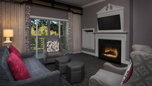 Una sala de estar con chimenea, un sofá, una silla y un ventanal con cortinas.