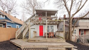 A two-story house with a covered deck, a red door, and a staircase leading to the upper floor. - Charming Hideaway in Westport 15 (KCMO)