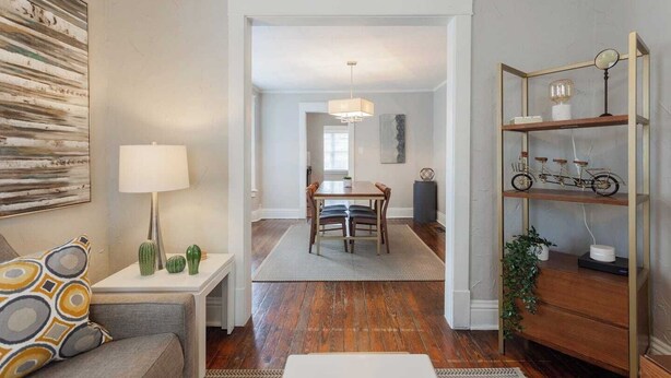 A modern living room with a sofa, a coffee table, and a lamp. There is a dining area with a table and chairs in the background. - Charming Hideaway in Westport 15 (KCMO)