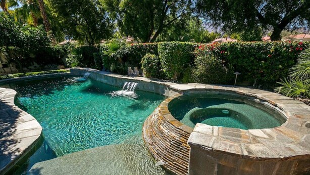 A swimming pool with a hot tub, surrounded by lush greenery and stone walls. - Villa Puerta Azul · Backyard Oasis at Puerta Azul (La Quinta)