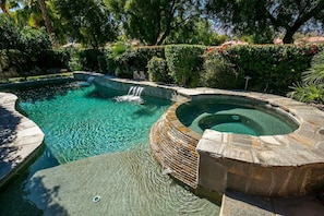 A swimming pool with a hot tub, surrounded by lush greenery and stone walls.
