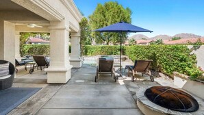 A covered patio with outdoor seating, a fire pit, and a view of a mountain range. - Villa Puerta Azul · Backyard Oasis at Puerta Azul (La Quinta)