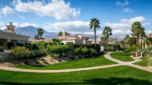 A well-maintained golf course with a clear pathway, surrounded by lush greenery and palm trees, leading to a building with a traditional architectural style. - Villa Puerta Azul · Backyard Oasis at Puerta Azul (La Quinta)