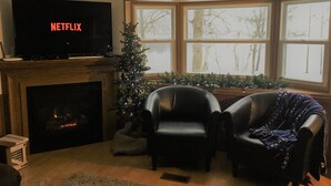 A living room with a fireplace, a television displaying 'NETFLIX', and a Christmas tree. - Cozy family & pet friendly lake home, great reviews & rates (Holcombe)