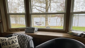A room with a view of a lake, a chair with a pillow, and a stack of suitcases on a windowsill. - Cozy family & pet friendly lake home, great reviews & rates (Holcombe)