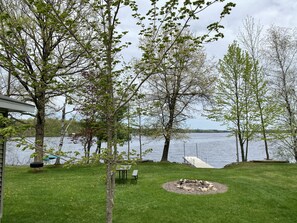 En ejendom ved søen med græsplæne, bålsted, picnicbord og en anløbsbro, der strækker sig ud i vandet.