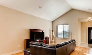 Relax in this spacious living room with a high ceiling, featuring a comfortable sofa and a large window with blinds.