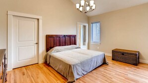 A bedroom with a wooden floor, a bed with a headboard, a chandelier, a window with blinds, and a wicker chest. - 60 Minutes to Ski Country, 15 Minutes to Downtown Denver (Golden)