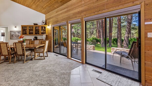 Een houten interieur met een eethoek, schuiframen naar een terras en uitzicht op een bebost gebied.