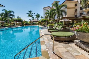 A swimming pool with lounge chairs and umbrellas, surrounded by palm trees and a multi-story building. - Beachfront Beach Villas at Ko Olina O-501 (Kapolei)