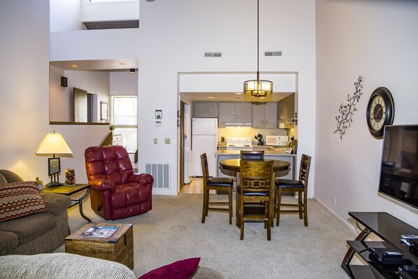 A living room with a red leather chair, a wooden dining table with chairs, a TV, and a lamp.