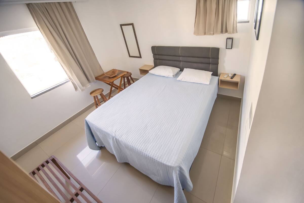 A bedroom with a large bed, a small table, two chairs, a nightstand, and a window with curtains.