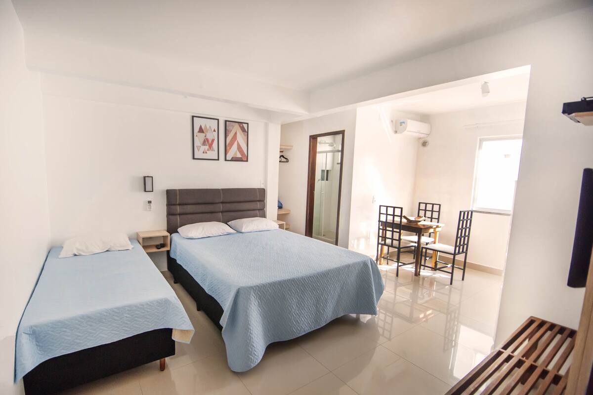 A hotel room with two beds, a dining area, and a bathroom.