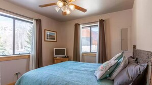 A bedroom with a bed, a ceiling fan, a TV on a small table, and windows with curtains. - The perfect place for outdoor recreation (Thayne)