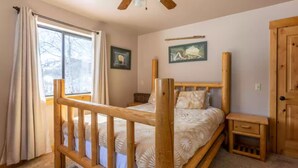 A bedroom with a wooden bed, a nightstand, a window with curtains, and a ceiling fan. - The perfect place for outdoor recreation (Thayne)