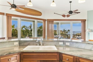 Una cocina moderna con una isla grande, armarios empotrados y un amplio ventanal con vistas a una piscina y palmeras.