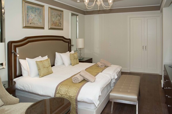 A hotel room with a large bed, a bedside table, a chair, a bench, and a wardrobe.